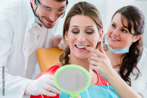 Frau nach Zahnbleaching beim Zahnarzt kontrolliert Zähne im Spiegel