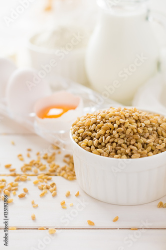 Ingredients for baking: flour, milk, wheat grain, butter and eggs on white wooden background. Selective focus 