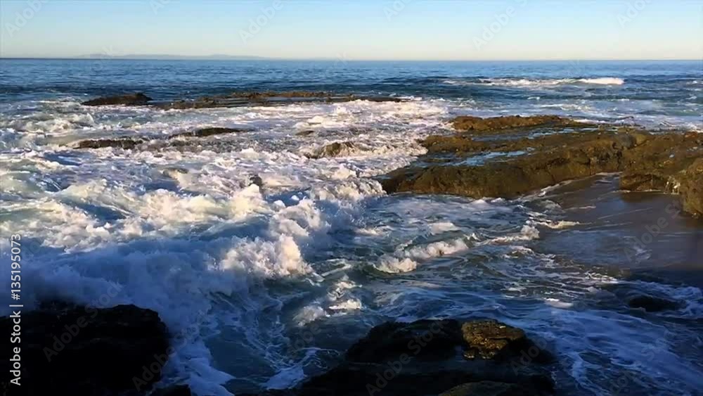 Waves shown in slow motion along a rocky beach crash and swirl over a shallow offshore reef system during a morning sunrise. Waves shown in slow motion along a rocky beach crash and swirl over a shallow offshore reef system during a morning sunrise.