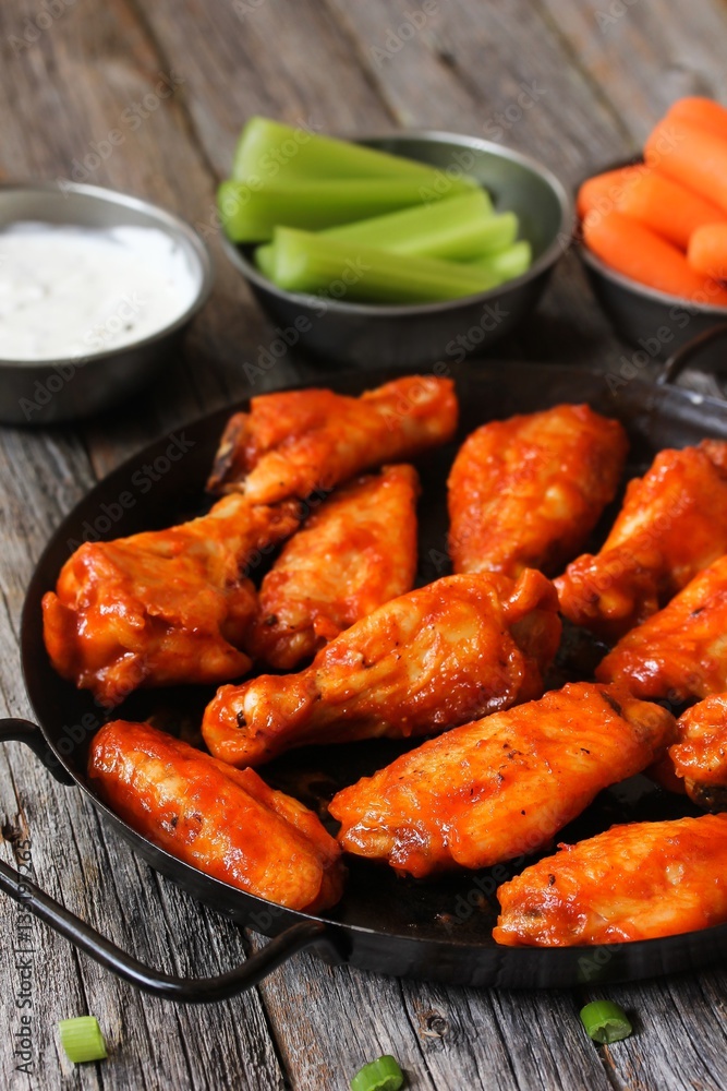Homemade spicy Buffalo chicken wings served with blue cheese dip celery sticks and baby carrots on rustic wooden background