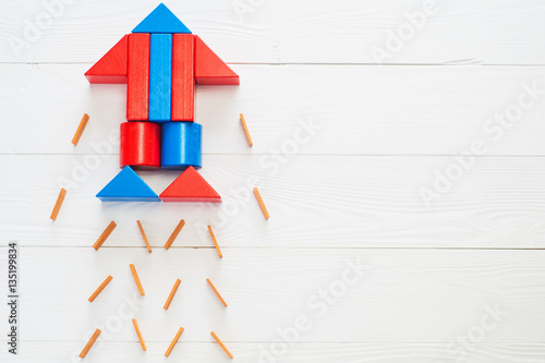 Abstract rocket from colored wooden blocks on a white wooden background with copy space. Business concept, startup, achievement, success. Wooden puzzle in rocket shape, discovery concept