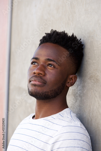 pensive adfrican man leaning on wall looking away