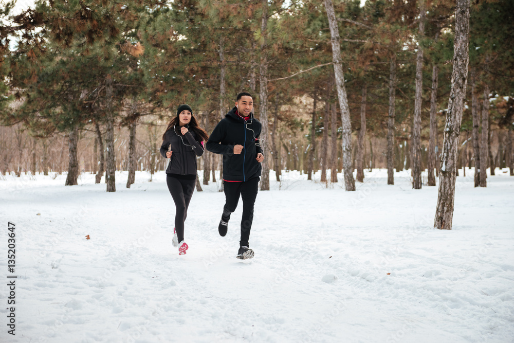 Healthy young couple jogging outside on snow in forest