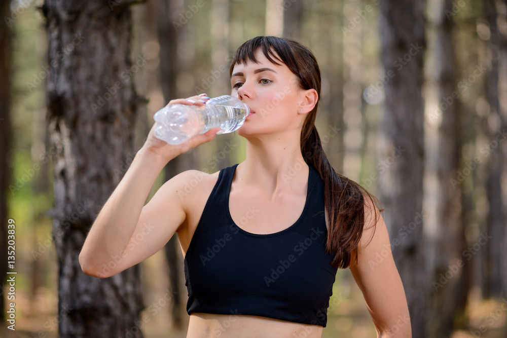 Young Sport Woman Drinking Water During Running in Beautiful Wild Pine Forest. Active Lifestyle Concept. Young Sport Woman Drinking Water During Running in Beautiful Wild Pine Forest. Active Lifestyle Concept.