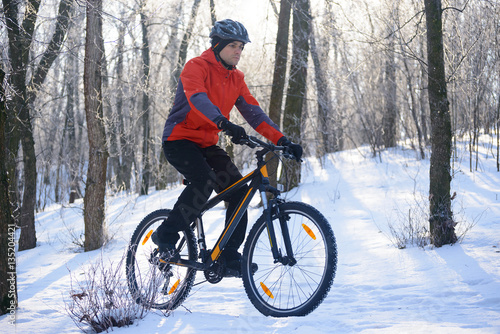 Mountain Biker Riding Bike on the Snowy Trail in the Beautiful Winter Forest Lit by Sun