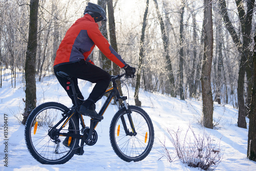 Mountain Biker Riding Bike on the Snowy Trail in the Beautiful Winter Forest Lit by Sun