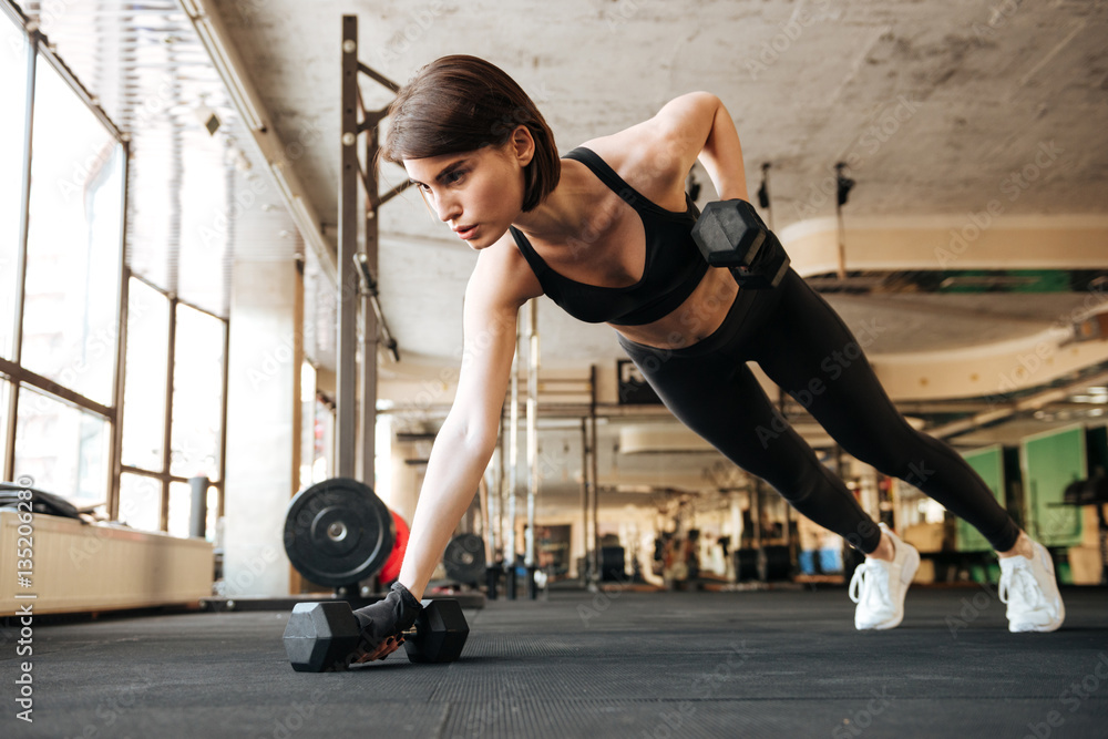Fototapeta premium Woman athlete doing exercises with dumbbells in gym