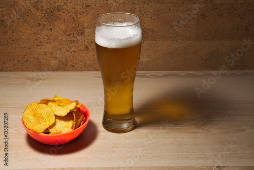 A pint of cold beer with a bowl of chips on a wooden table