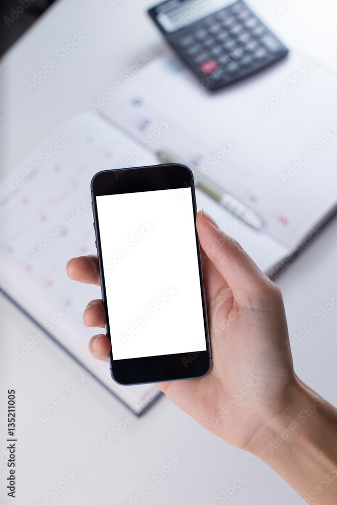 A female hand holding smart phone with office stationeries at working desk A female hand holding smart phone with office stationeries at working desk
