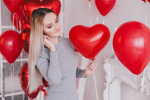 Beautiful young woman posing with red heart balloons in a white room. Valentine's Day