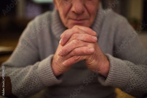 Unrecognizable senior man at home praying, hands clasped togethe
