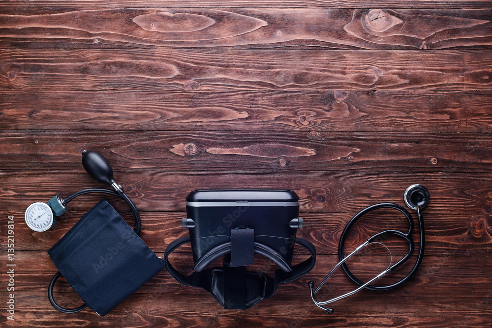 Tonometer,VR glasses and stethoscope.Top view/Blood pressure cuff,virtual reality glasses and stethoscope on wooden table Tonometer,VR glasses and stethoscope.Top view/Blood pressure cuff,virtual reality glasses and stethoscope on wooden table