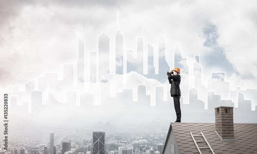 Engineer man standing on roof and looking in binoculars. Mixed m Engineer man standing on roof and looking in binoculars. Mixed m