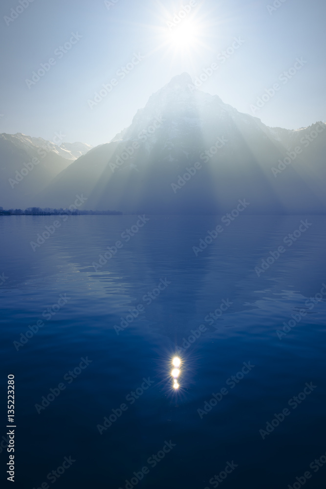  Shape in nature. Sunrays over the top of the mountains reflected in the lake. Play of light and shadow creates volume pyramid shape.