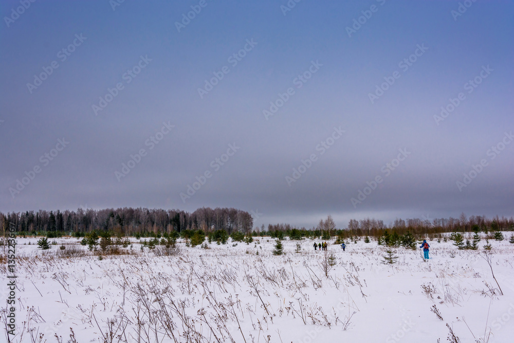 Tourists walk along a snow-covered winter field.