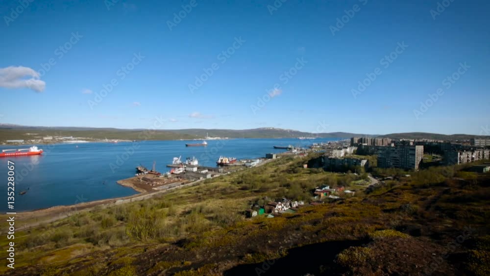 Panoramic View From the Hilly Area on the City Buildings and Navigable River in Murmansk. Sunny Sammer Day. Blue Cloudy Sky. Vessels Are on the Water Panoramic View From the Hilly Area on the City Buildings and Navigable River in Murmansk. Sunny Sammer Day. Blue Cloudy Sky. Vessels Are on the Water