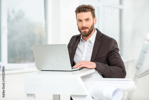 Architect or designer working with laptop on the ladder with paper drawings in the bright room for renovating