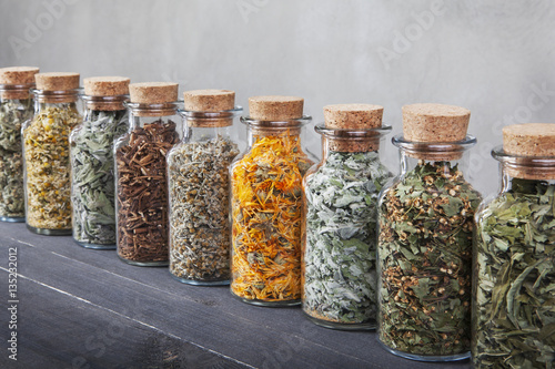 Different kinds of herbs for tea inside glass bottles.
