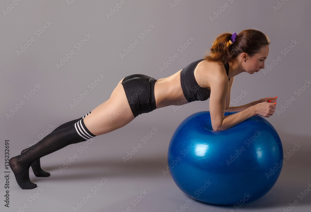 Obraz premium Young woman doing exercises with fitball, on a gray background.