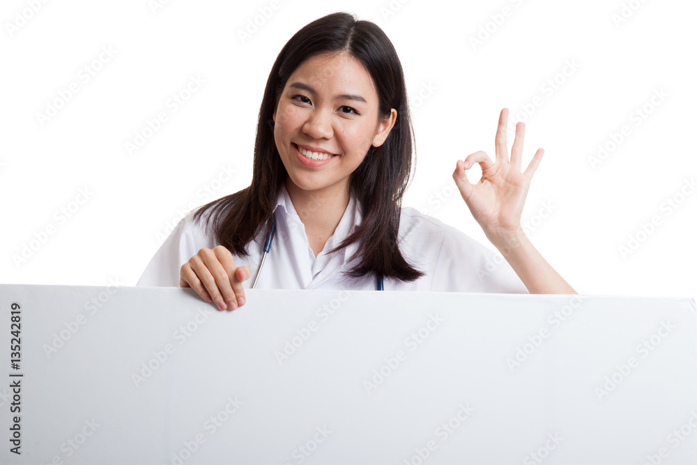 Young Asian female doctor show OK sign behind blank white billb Young Asian female doctor show OK sign behind blank white billb