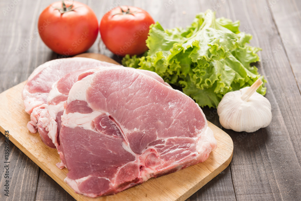 Raw pork on cutting board and vegetables on wooden background