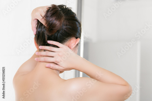 Woman in bathroom looking in to mirror and bundle on her hair.