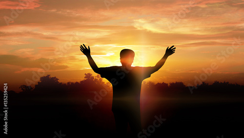 A man raising arms in sunset.