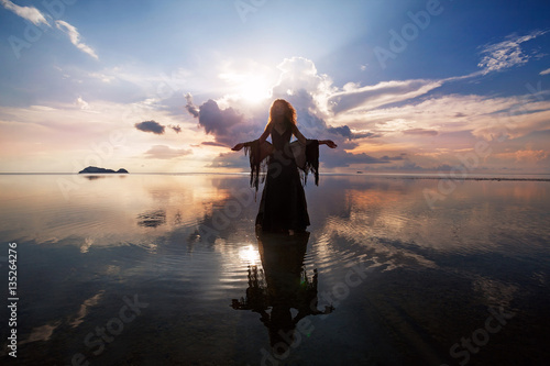Canvas Print Elegant woman walking on water. Sunset and silhouette.