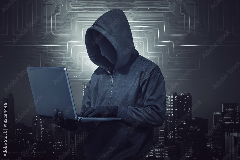 Hooded hacker holding laptop while typing Hooded hacker holding laptop while typing