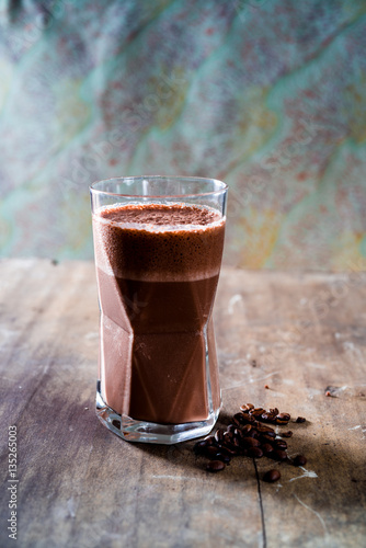 Spicy, frothy chili coffee smoothie and whole coffee beans on a textured wooden surface with patterened light blue, red and yellow background. photo