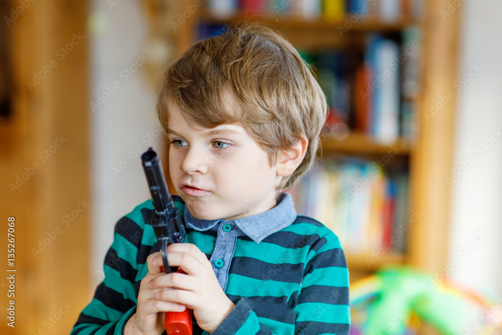 Cute little preschool kid boy playing with gun at home,