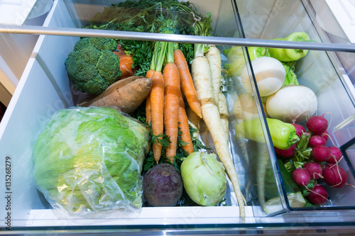 Open fridge , drawer filled with fresh vegetables