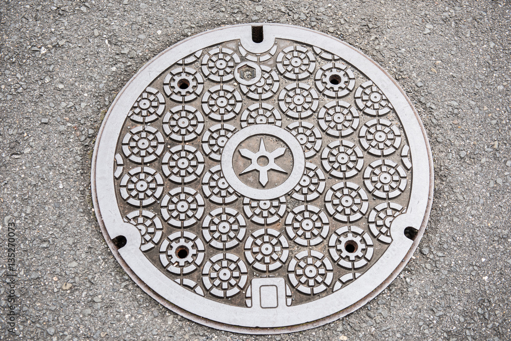 In the picture we can see a circular design of a classic art on a manhole cover. The art looks very neat and clean. It is made of steel and concrete.