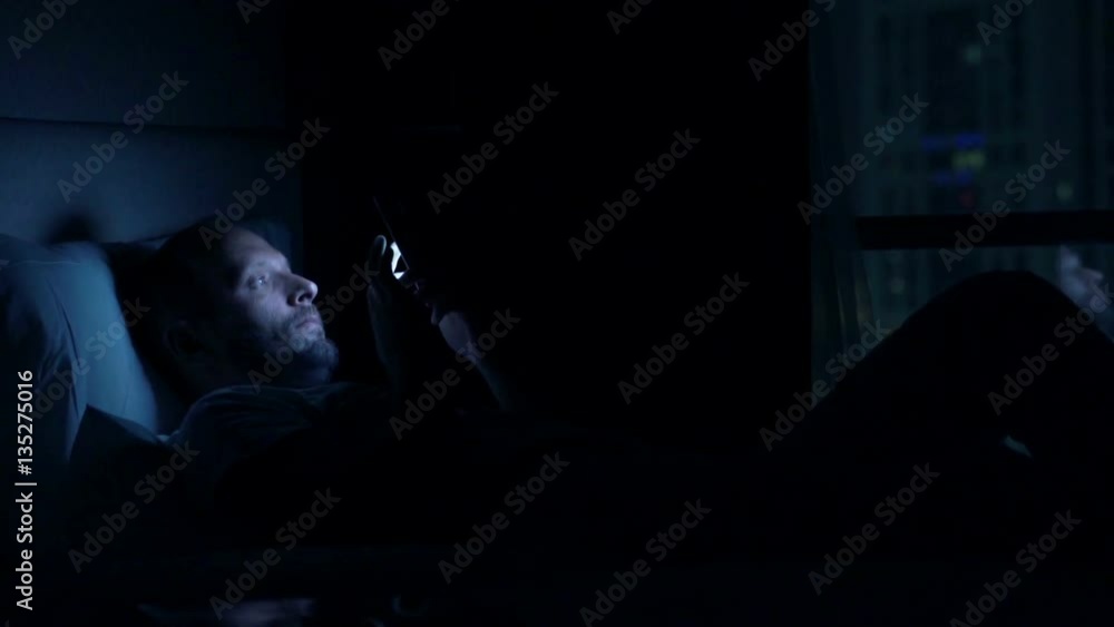 Man waking up and using smartphone on bed at home at night
Man waking up and using smartphone on bed at home at night