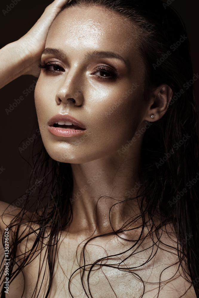 Beautiful girl with a bright make-up and wet hair and skin. Beauty face. Picture taken in the studio on a black background.
