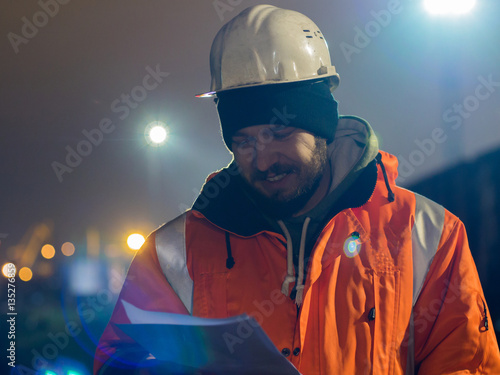 Portrait of young and happy construction worker in helmet at night.