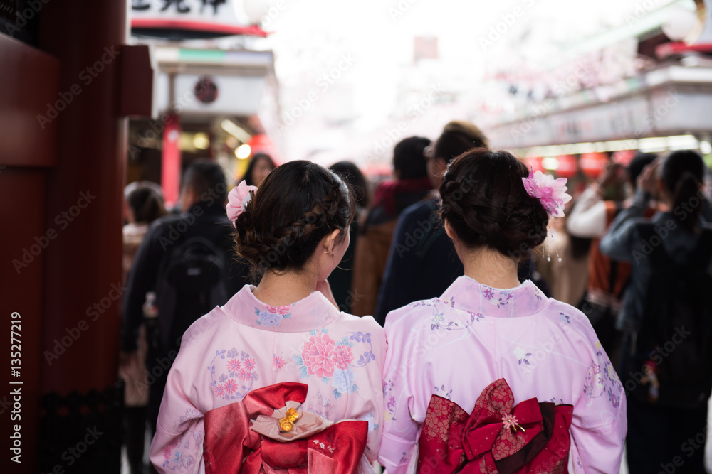 Couple Japanese women in traditional attires visiting a sacred buddhist temple in Tokyo. On the background, parts of the shrine and crowds of people are seen.