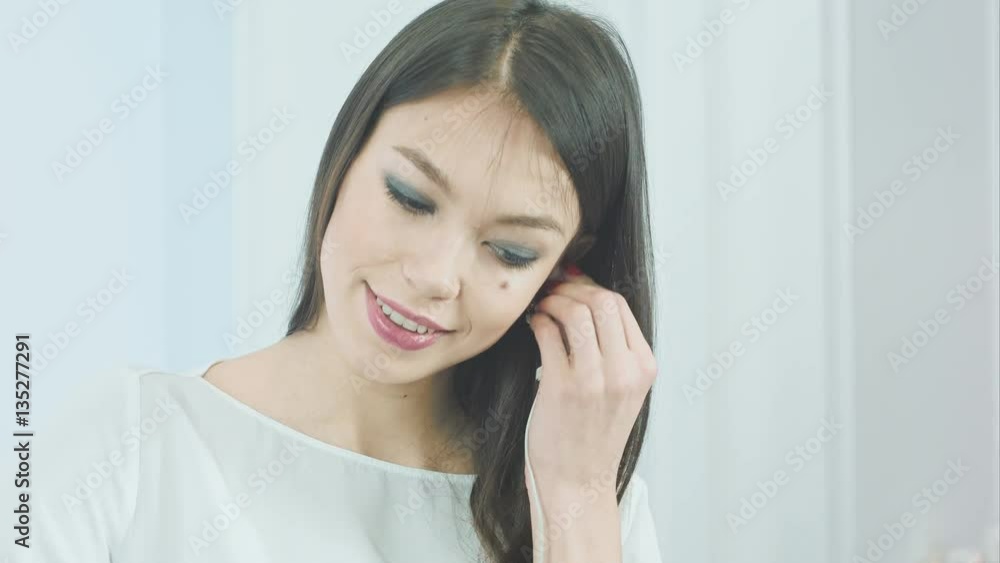 Pretty young woman inserting white earphones into her ears to listen to the music Pretty young woman inserting white earphones into her ears to listen to the music