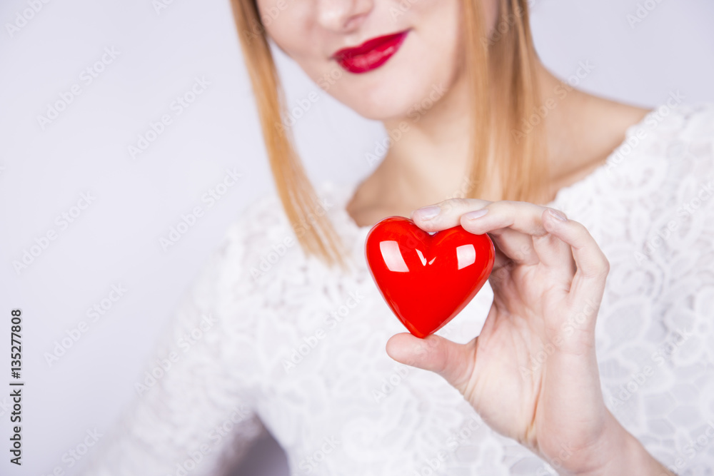 Smiling beautiful red-haired woman holding red heart on white ba Smiling beautiful red-haired woman holding red heart on white ba