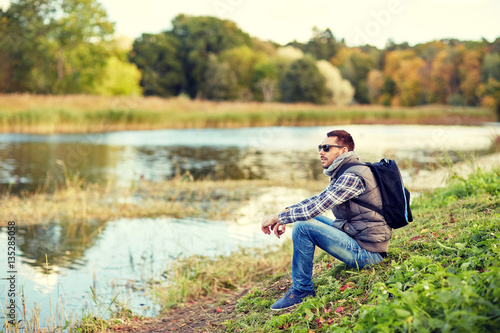 man with backpack resting on river bank