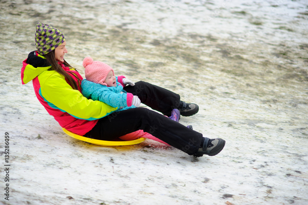 Obraz premium Young woman with little daughter together move down from a hill on saucer sled.