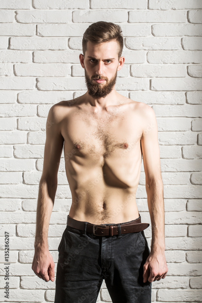 slim bearded man with thin bare torso on brick background
