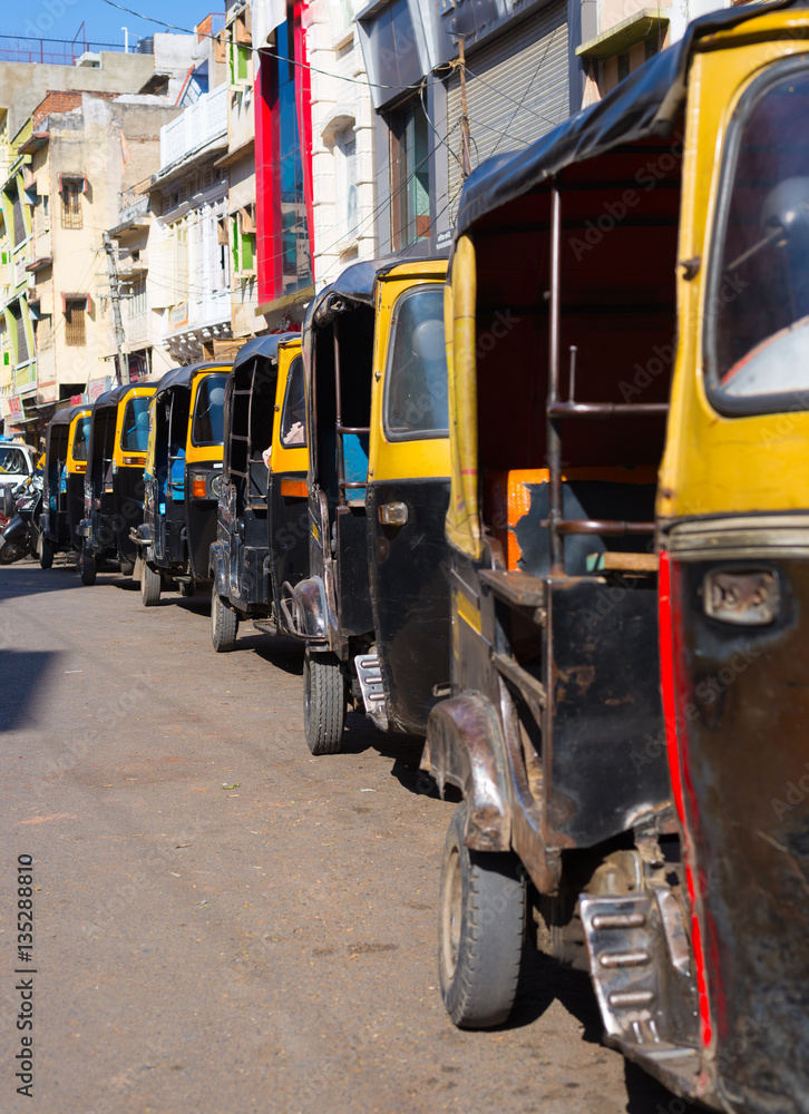 Obraz premium Yellow black rickshaws (tuk tuk) lined up in the street of Udaipur, Rajasthan, India.