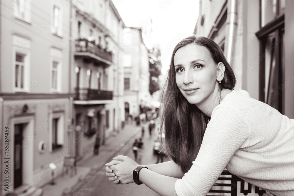 Young beautiful woman standing on the balcony and looking out on street of european city Young beautiful woman standing on the balcony and looking out on street of european city