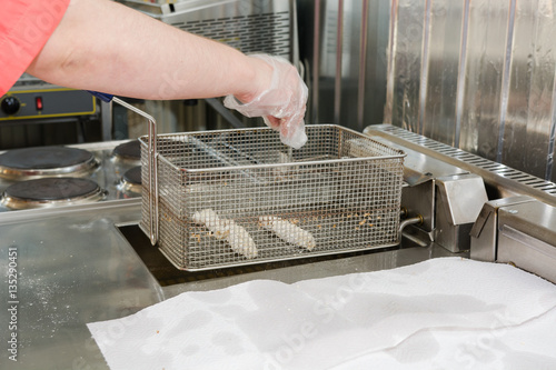 The cook fries meat in a deep fryer.