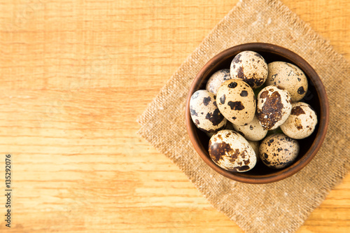 Quail eggs in a bowl on sacking on a wooden surface