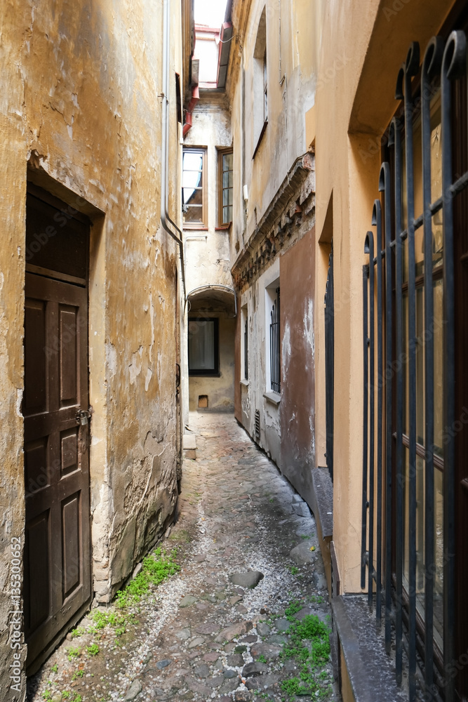 Fototapeta premium Narrow passage between buildings. Old walls with cracked paint. Explore an old town.