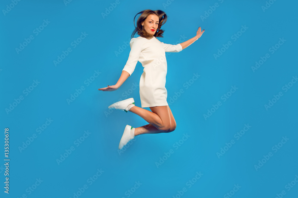 cheerful girl in a white dress and sneakers posing in a jump
