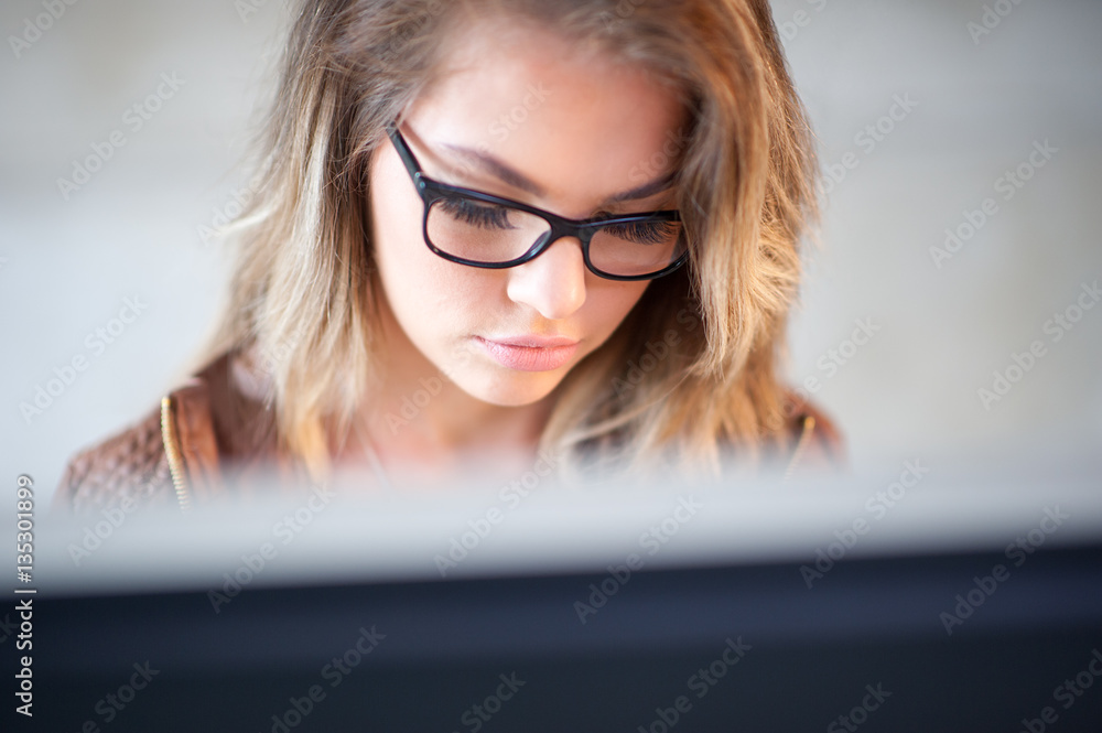 Beautiful young woman sitting at her desk working on a computer. Beautiful young woman sitting at her desk working on a computer.