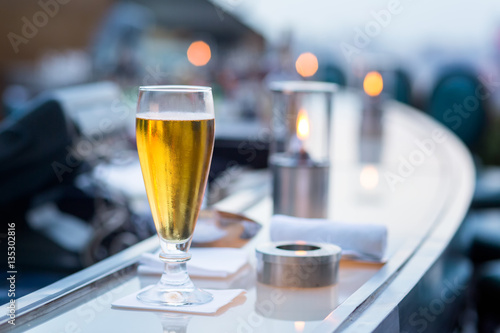 Photography Glass of beer in Bangkok city view point from rooftop of building, blue sky and city light, Bangkok is the most populated city in Southeast Asia